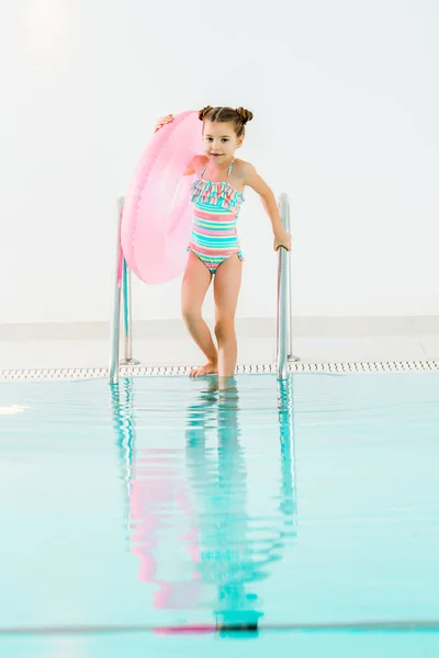 Adorable enfant avec anneau gonflable tenant la main courante dans la piscine — Photo de stock