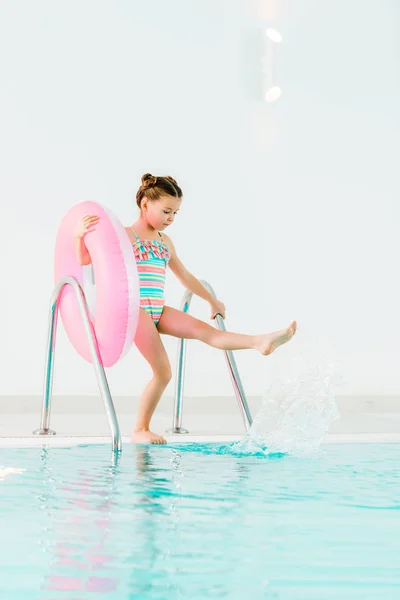 Adorable kid in swimwear holding inflatable ring and playing with water in swimming pool — Stock Photo