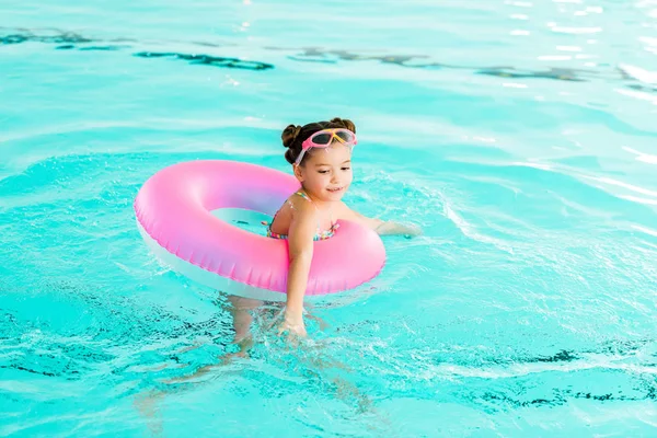 Щаслива дитина в окулярах вчиться плавати з надувним кільцем у басейні — стокове фото