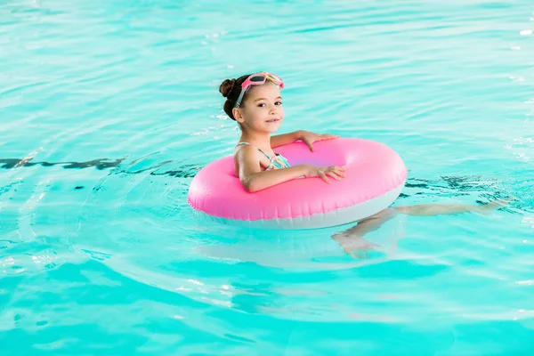 Kid in googles learning swimming with inflatable ring in swimming pool — Stock Photo