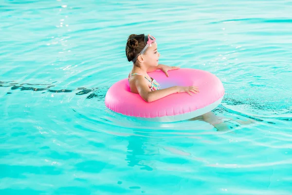 Criança em googles aprendendo a nadar com anel inflável na piscina — Fotografia de Stock