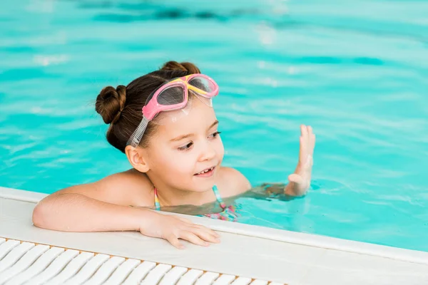 Cute kid in googles swimming near poolside in swimming pool — Stock Photo