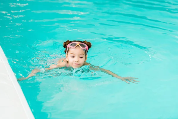 Мила дитина в окулярах вчиться плавати у блакитній воді в басейні — стокове фото