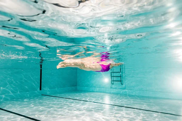 Mujer buceando bajo el agua en traje de baño rosa en la piscina - foto de stock