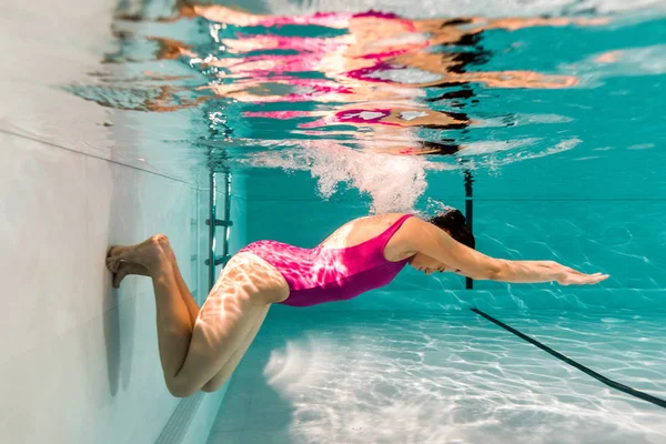 Mujer buceando bajo el agua en traje de baño rosa en agua azul en la piscina - foto de stock