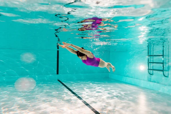 Mujer buceando bajo el agua en traje de baño rosa en agua azul de la piscina - foto de stock