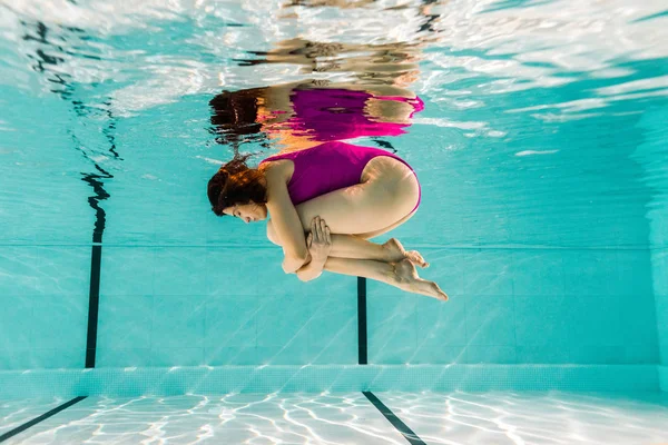 Mujer sosteniendo las piernas mientras bucea bajo el agua en la piscina - foto de stock