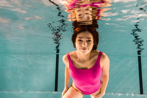Atractiva mujer sonriendo mientras nada en agua azul en la piscina - foto de stock