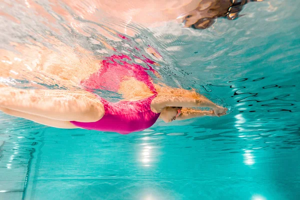 Жінка плаває в рожевому купальнику під водою в басейні — стокове фото