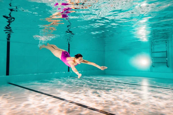 Mujer nadando en traje de baño rosa y googles bajo el agua - foto de stock