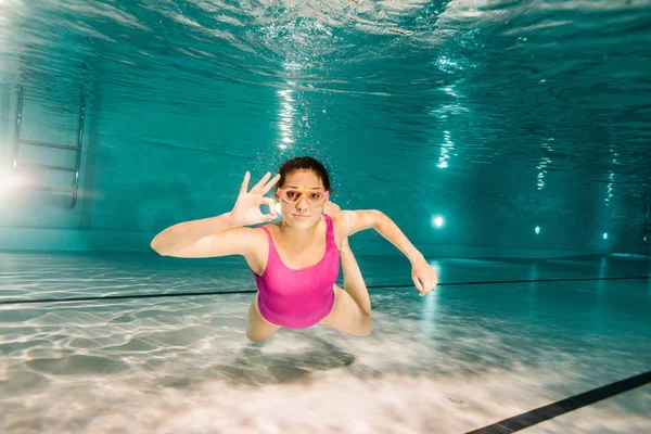 Жінка в окулярах показує знак ОК під час дайвінгу під водою — стокове фото
