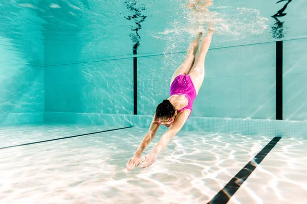 Жінка занурюється під воду в басейн з блакитною водою — стокове фото