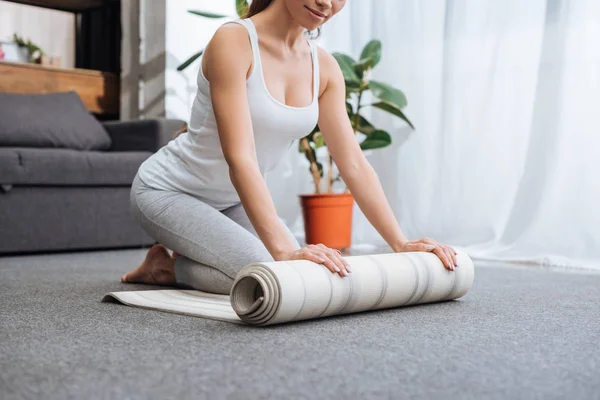 Abgeschnittene Ansicht einer Frau, die Fitnessmatte rollt, um zu Hause Yoga zu praktizieren — Stockfoto