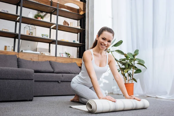Foco seletivo de mulher sorridente rolando tapete de fitness para praticar ioga em casa — Fotografia de Stock