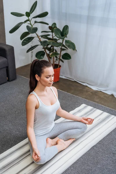 Selektiver Fokus der schönen jungen Frau, die in Lotuspose sitzt und zu Hause meditiert — Stockfoto