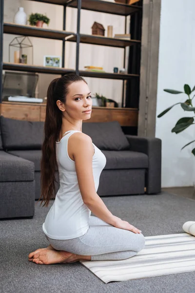 Schöne Frau sitzt auf Fitnessmatte und übt sich zu Hause in Heldenpose — Stockfoto