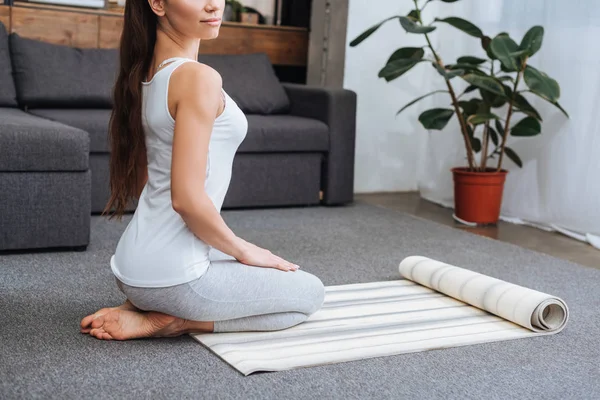 Vista recortada de la mujer sentada en la alfombra de fitness y la práctica de pose héroe en casa - foto de stock