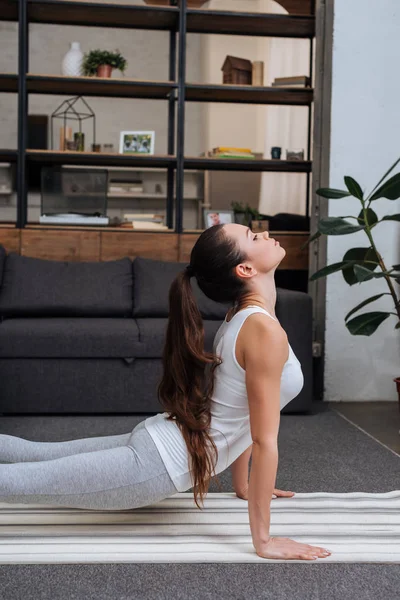 Selective focus of young woman practicing cobra pose in living room at home — Stock Photo