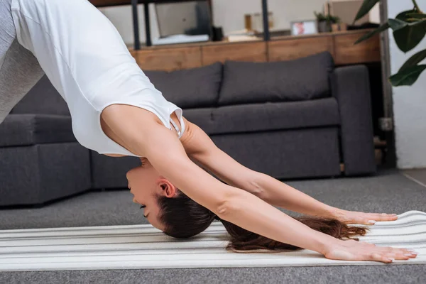 Selective focus of young woman practicing downward facing dog pose at home — Stock Photo