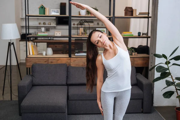 Beautiful young woman doing stretching exercise at home in living room — Stock Photo