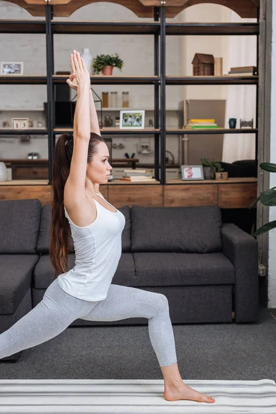 Focused young woman practicing warrior pose at home in living room — Stock Photo