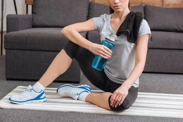 Cropped view of sportswoman with towel and sport bottle sitting in living room — Stock Photo