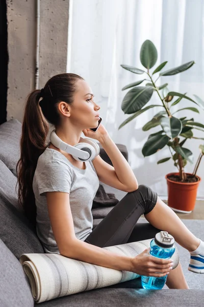Attractive sportswoman with headphones talking on smartphone at home — Stock Photo