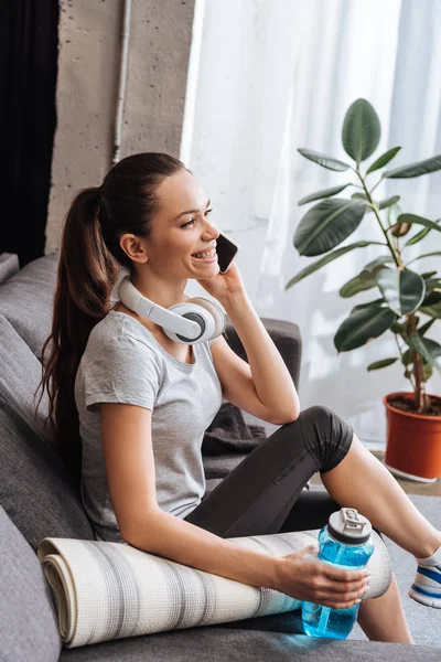 Sportive souriante avec écouteurs parlant sur smartphone à la maison — Photo de stock