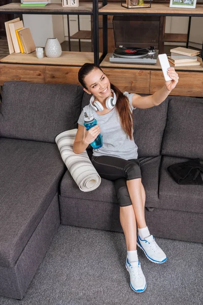 Belle sportive heureuse avec écouteurs prenant selfie sur smartphone à la maison — Photo de stock
