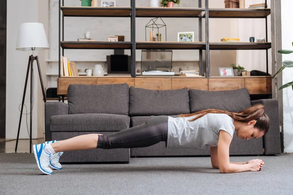 Целенаправленная спортсменка, выполняющая упражнения на доске дома в гостиной — стоковое фото