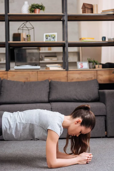 Sportive ciblée faisant de l'exercice de planche à la maison dans le salon — Photo de stock