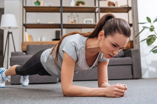 Selective focus of beautiful concentrated sportswoman doing plank exercise at home — Stock Photo