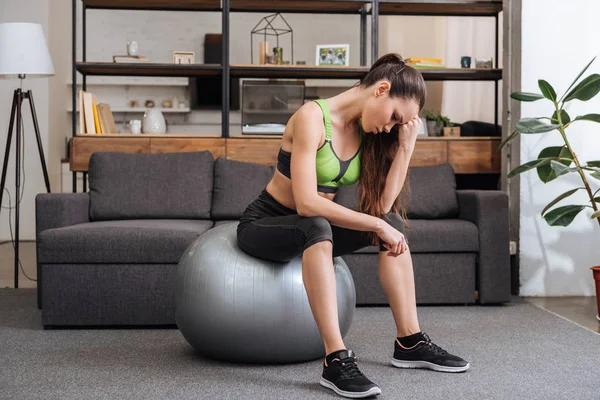 Tired sportswoman sitting on fitness ball at home in living room — Stock Photo