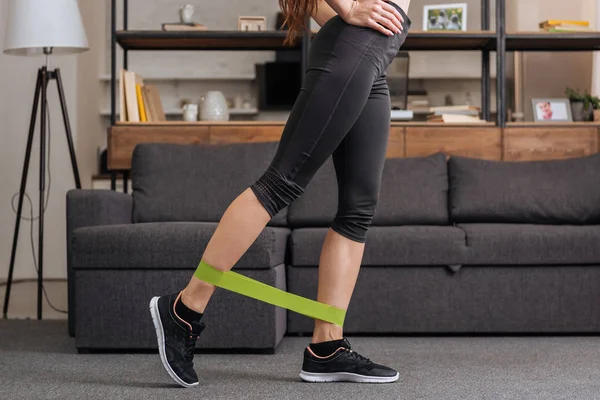 Low section of sportswoman training with resistance band at home in living room — Stock Photo