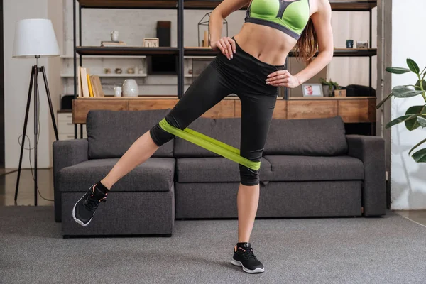 Partial view of sportswoman training with resistance band at home in living room — Stock Photo