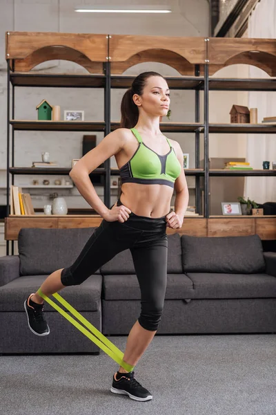 Beautiful concentrated sportswoman training with resistance band at home in living room — Stock Photo