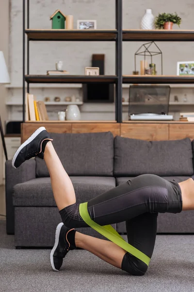 Cropped view of sportswoman training with resistance band at home in living room — Stock Photo