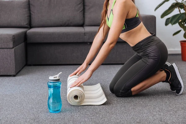 Partial view of athletic sportswoman with fitness mat and sport bottle at home — Stock Photo