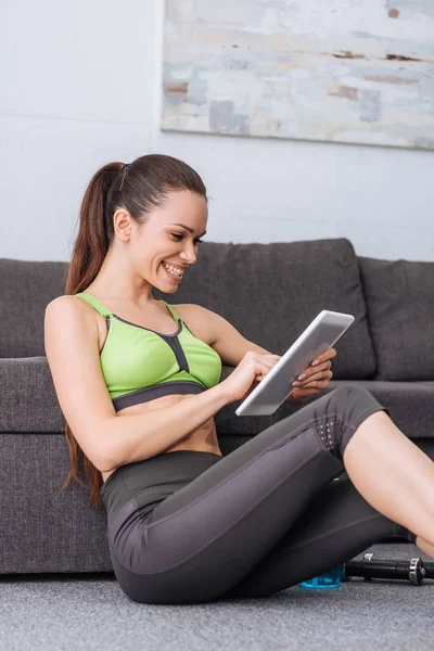 Усміхнена спортсменка сидить і використовує цифровий планшет вдома — стокове фото