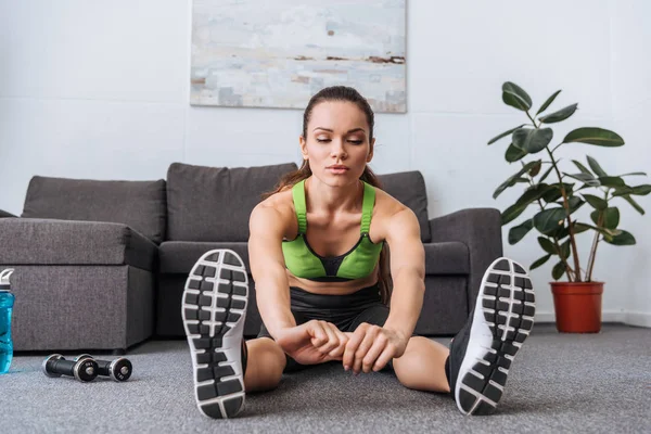 Sportiva seduta e fare esercizio di stretching a casa — Foto stock