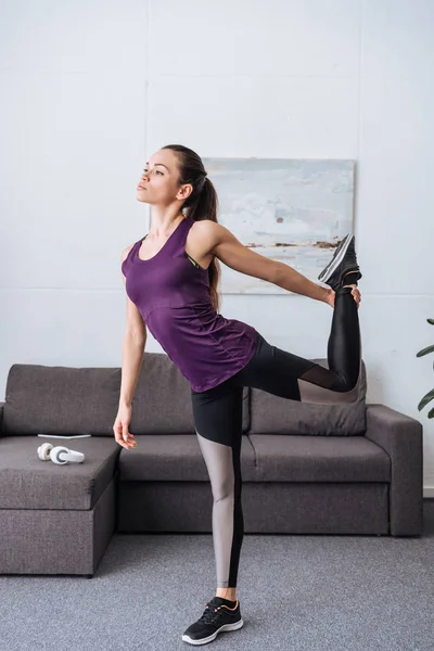 Beautiful young sportswoman stretching before workout at home — Stock Photo