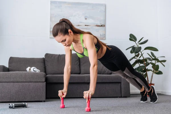 Fokussierte Sportlerin macht Liegestütze mit Hanteln zu Hause — Stockfoto