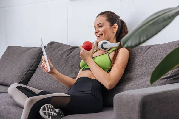 Deportista con auriculares que sostiene la manzana y el uso de la tableta digital en casa - foto de stock