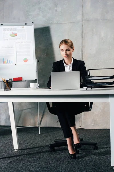 Jeune femme d'affaires concentrée utilisant un ordinateur portable dans le bureau avec conseil d'administration sur fond — Photo de stock