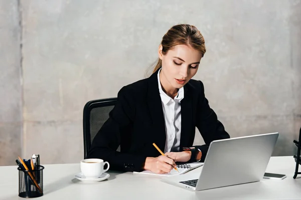 Junge konzentrierte Geschäftsfrau sitzt am Arbeitsplatz und macht sich Notizen — Stockfoto