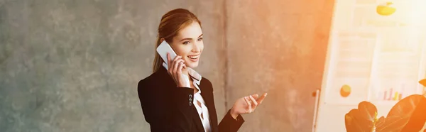 Atractiva mujer de negocios sonriente hablando en el teléfono inteligente en la oficina - foto de stock