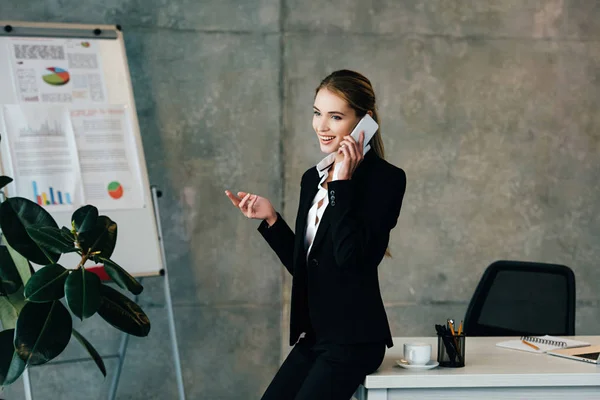 Sorridente empresária falando no smartphone enquanto em pé por mesa de trabalho — Fotografia de Stock