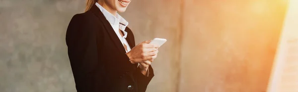 Vista recortada de una mujer de negocios sonriente usando un teléfono inteligente en la oficina - foto de stock