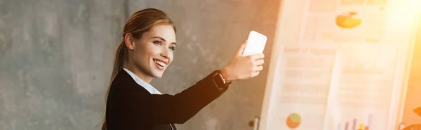Smiling beautiful businesswoman taking selfie in office — Stock Photo