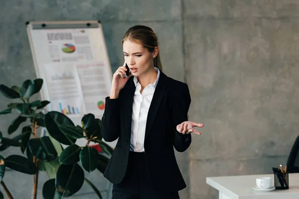 Mujer de negocios seria hablando en el teléfono inteligente en la oficina - foto de stock